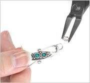 split ring pliers gripping a split ring and a hand holding a turquoise piece connected to another split ring.